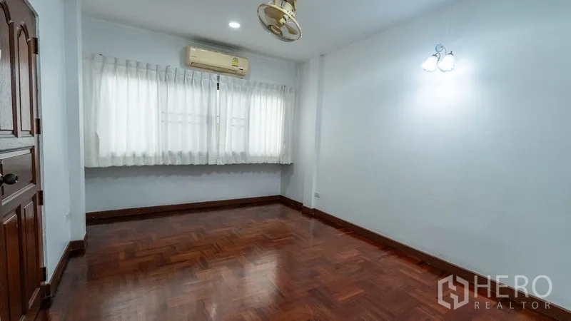 联排别墅 出租在Khlong Toei, Bangkok - 空调卧室，木地板与宽阔窗户挂有窗帘。