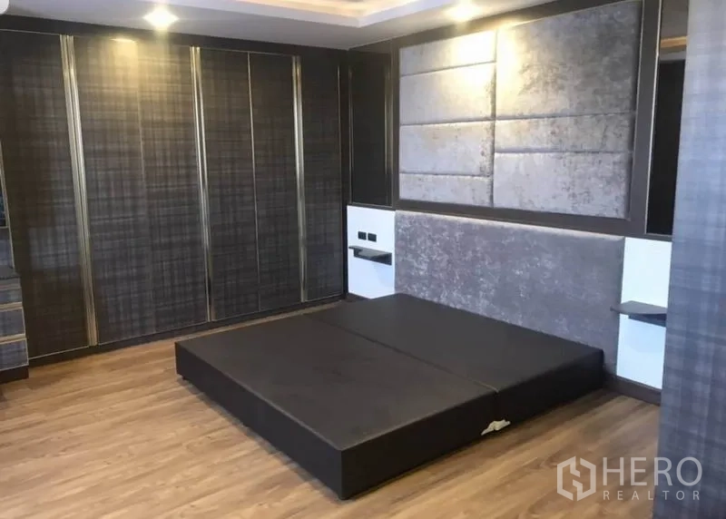 Condominium for rent in Khlong Toei, Bangkok - Spacious master bedroom with platform bed, feature wall and full-height wardrobes.