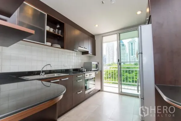 Apartment for rent in Sathon, Bangkok - Separate kitchen with dark wood cabinets, built-in oven and balcony door with city view.