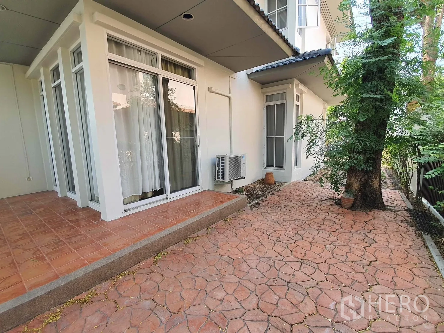 Detached House for rent in Wang Thonglang, Bangkok - Side patio with tiled terrace, sliding glass doors, and a shaded walkway beside a mature tree.