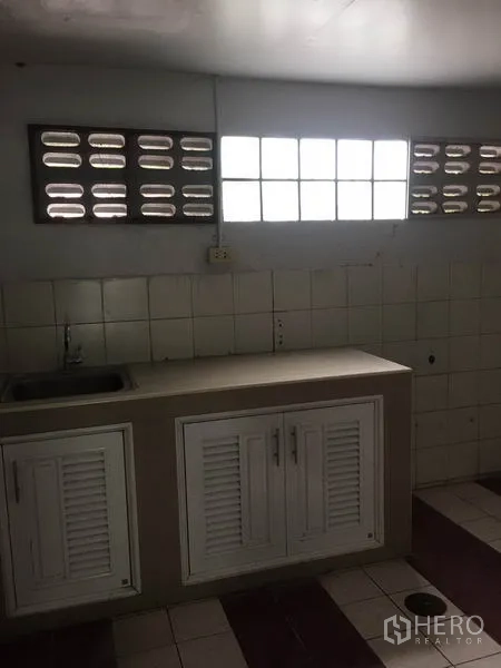 Shophouse for rent in Khlong Toei, Bangkok - Simple pantry with tiled wall, countertop, and louvered cabinets beneath vented windows.