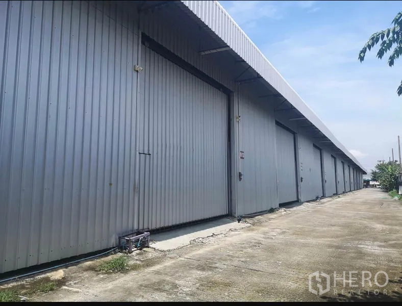 Warehouse for rent in Lam Luk Ka, Pathum Thani - Row of metal-clad warehouse units with large sliding doors and a wide concrete driveway.