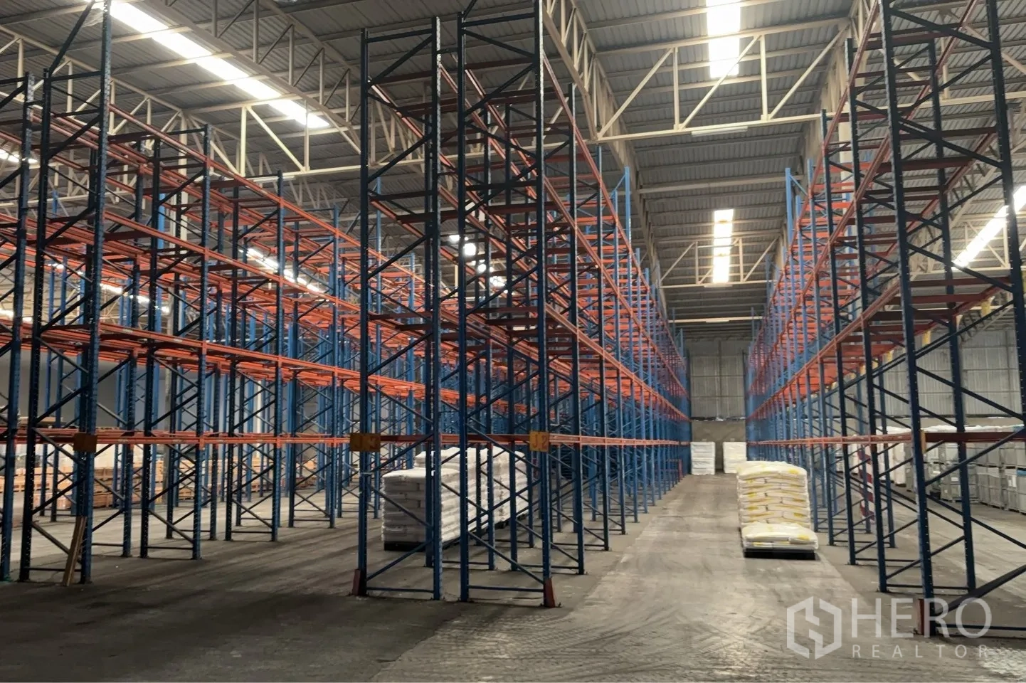 Warehouse for rent in Bang Pa-in, Phra Nakhon Si Ayutthaya - Wide warehouse aisle lined with tall racking systems and stacked bagged goods on pallets under high-bay lighting.