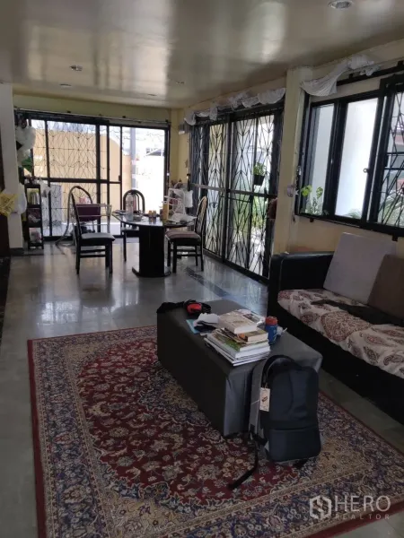 Townhouse for rent in Phra Khanong, Bangkok - Long living and dining area with multiple windows, metal grilles, sofa seating, and a patterned rug.