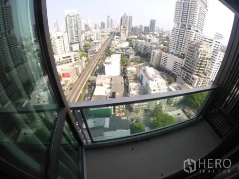 Condominium for rent in Khlong Toei, Bangkok - High-floor balcony overlooking the Sukhumvit skyline with BTS tracks visible below.
