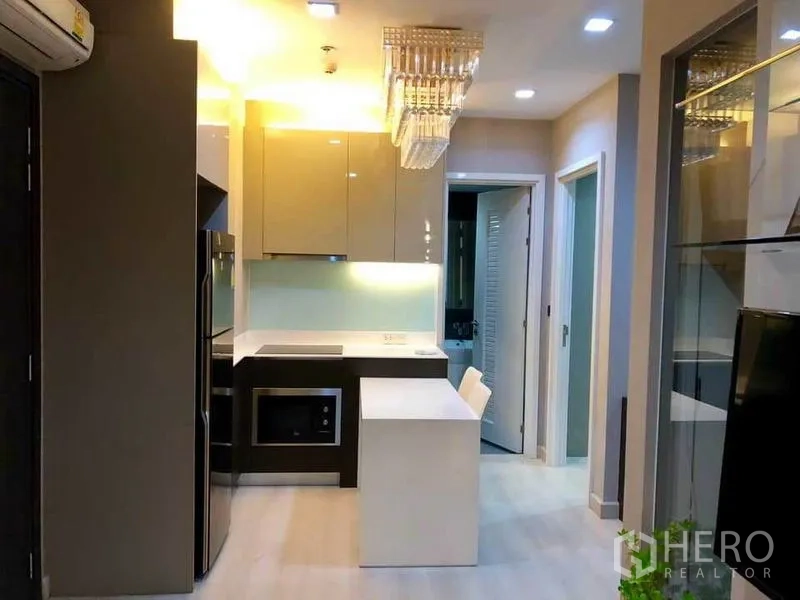 Condominium for rent or sale in Phaya Thai, Bangkok - Modern kitchenette with island, glossy cabinets and chandelier leading to the bedrooms.
