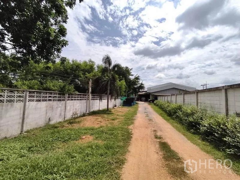 Factory for sale in Lat Lum Kaeo, Pathum Thani - Private access lane with perimeter walls and greenery leading to warehouse buildings in Lat Lum Kaeo.