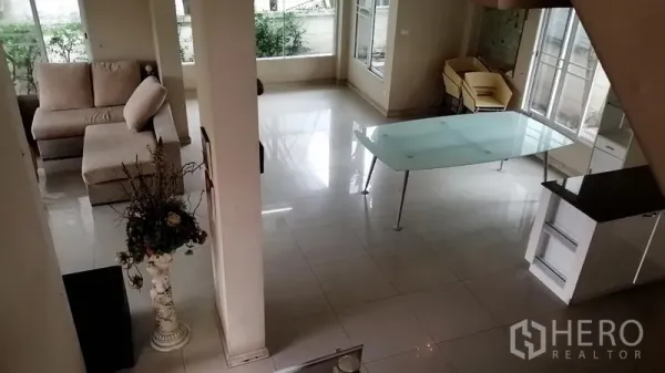 Detached House for rent in Lat Krabang, Bangkok - View from the staircase over the ground floor showing a glass dining table, sofa corner, and garden-facing windows.