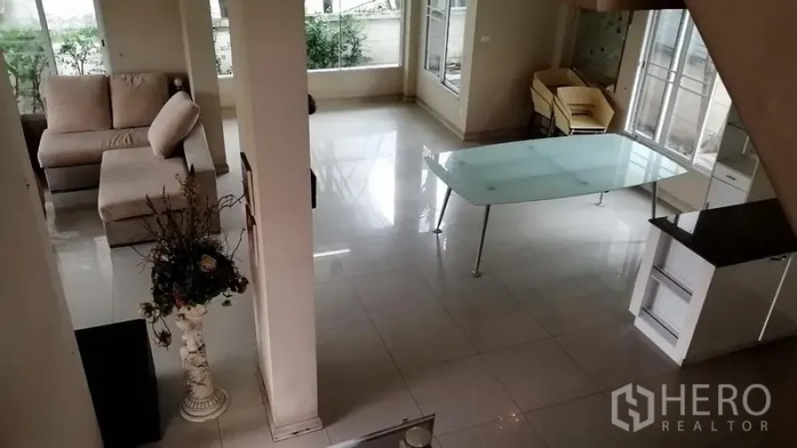 Detached House for rent in Lat Krabang, Bangkok - View from the staircase over the ground floor showing a glass dining table, sofa corner, and garden-facing windows.