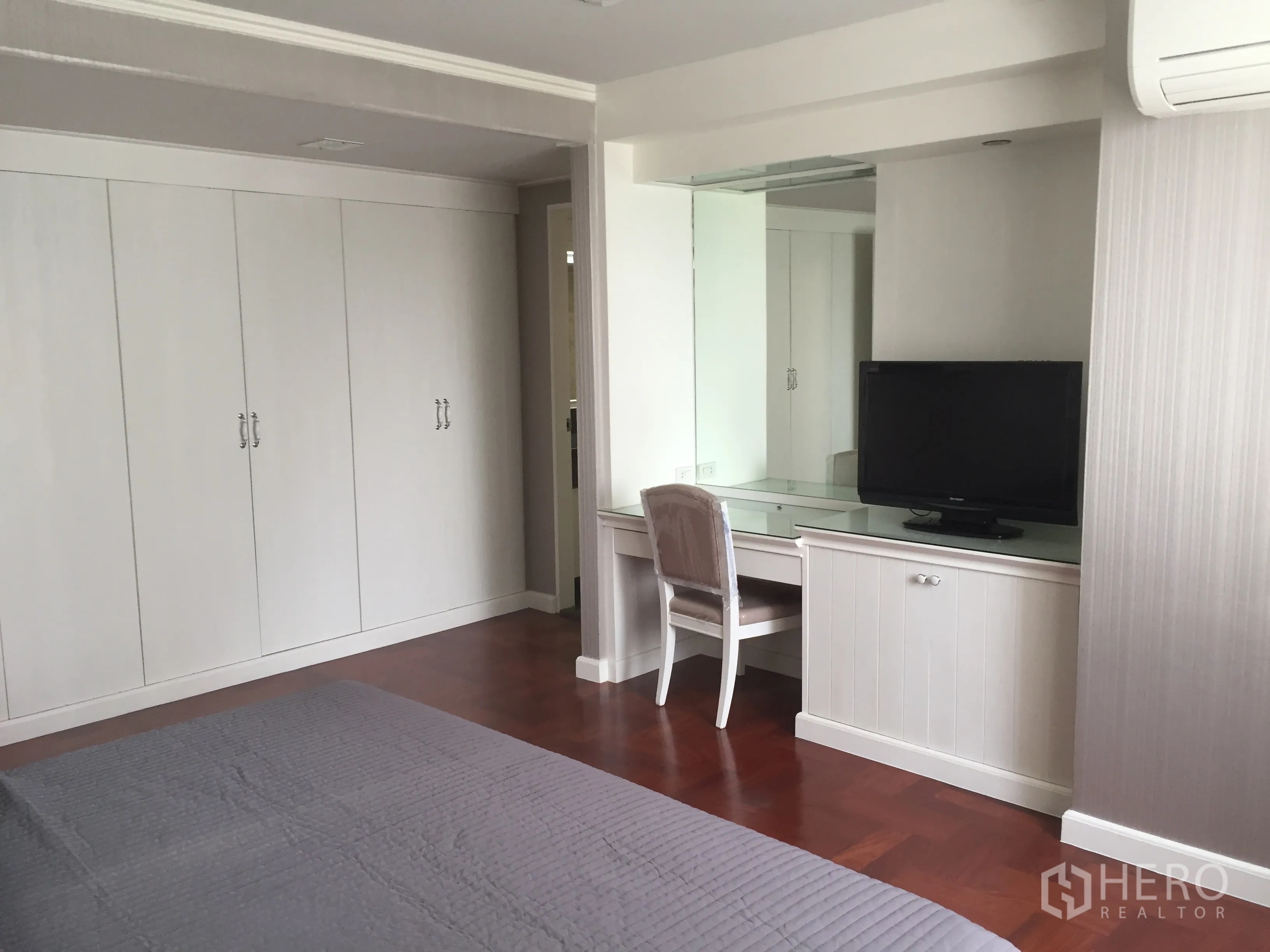Condominium for rent in Khlong Toei, Bangkok - Spacious bedroom featuring built-in white wardrobes, a dressing desk with TV, and warm wood flooring.