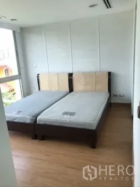 Townhouse for rent or sale in Yan Nawa, Bangkok - Second bedroom with twin beds, white walls and corner glazing.