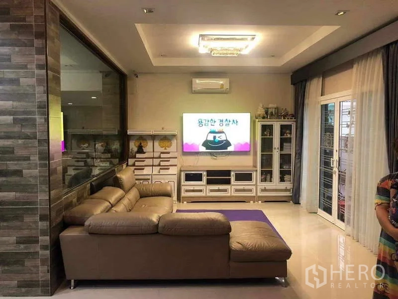 Detached House for rent or sale in Prawet, Bangkok - Cozy living room with sectional sofa, TV wall unit, cabinets and sliding doors.