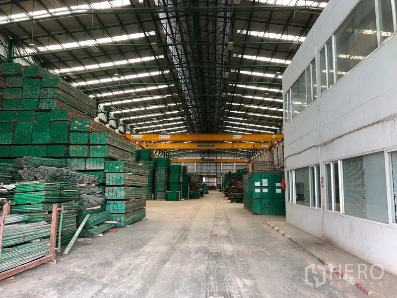 Factory for rent or sale in Lat Lum Kaeo, Pathum Thani - Warehouse corridor beside office wing with material stacks and overhead cranes.