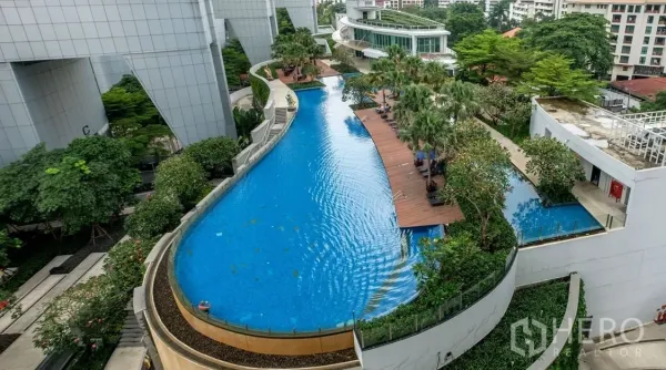 Condominium for rent or sale in Khlong Toei, Bangkok - Aerial view of a curving resort-style swimming pool with wooden sun deck and lush gardens at a modern Bangkok condo.