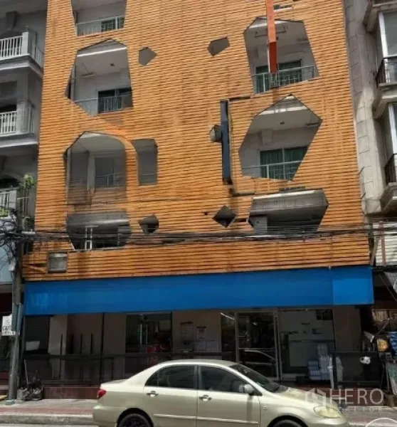 Retail Space for rent in Watthana, Bangkok - Four-storey mixed-use building with distinctive orange cladding and blue fascia, showing the ground-floor retail shopfront and street parking.