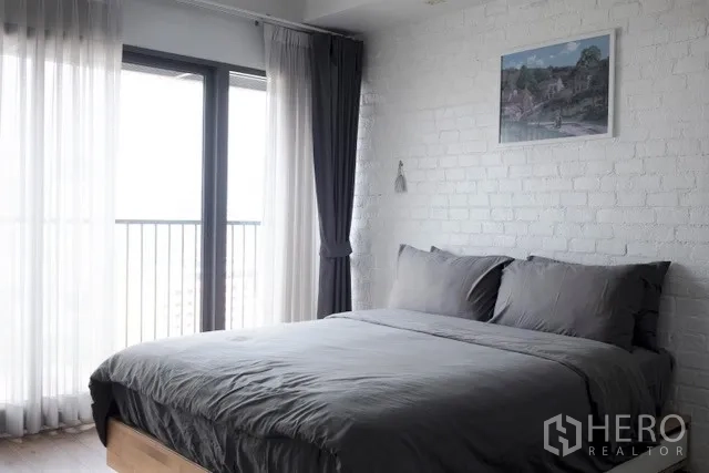 Condominium for rent in Khlong Toei, Bangkok - Bright bedroom with gray bedding, floor-to-ceiling windows, curtains and a balcony view.