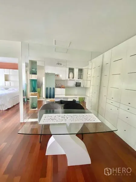 Condominium for rent in Watthana, Bangkok - Open-plan dining area featuring a glass table, modern built-in storage, mirrors, and polished wooden floors.