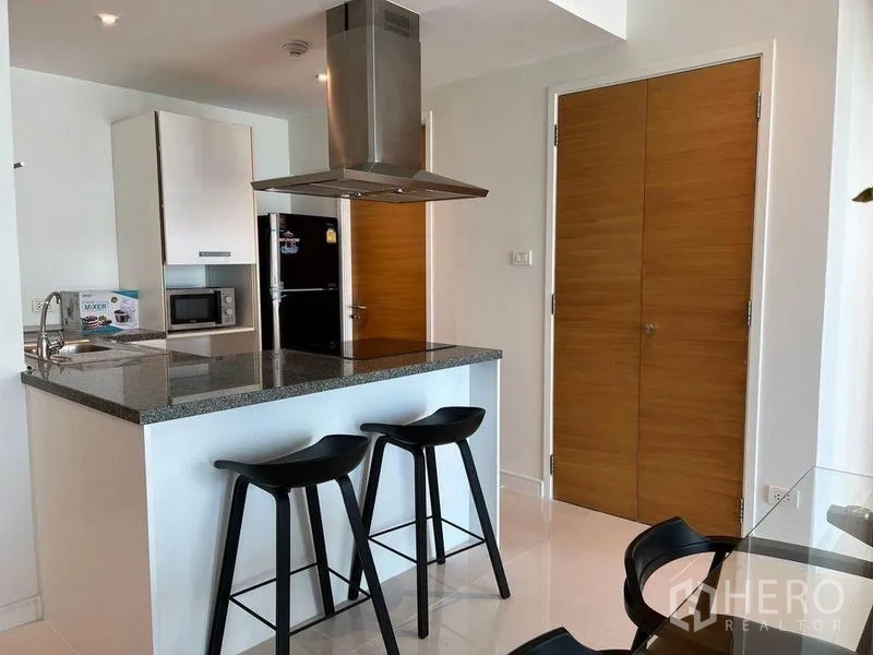 Condominium for rent in Watthana, Bangkok - Kitchen island with granite countertop, range hood, and bar stools.