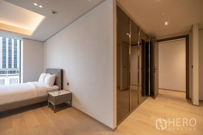 Condominium for rent in Pathum Wan, Bangkok - Bedroom with large window, bed and glossy wardrobes, city buildings outside.