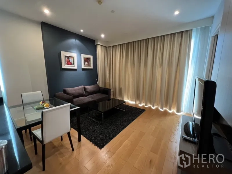 Condominium for rent in Chatuchak, Bangkok - Cozy living space with glass-top TV stand, large curtains, and dining nook beside the kitchen bar.