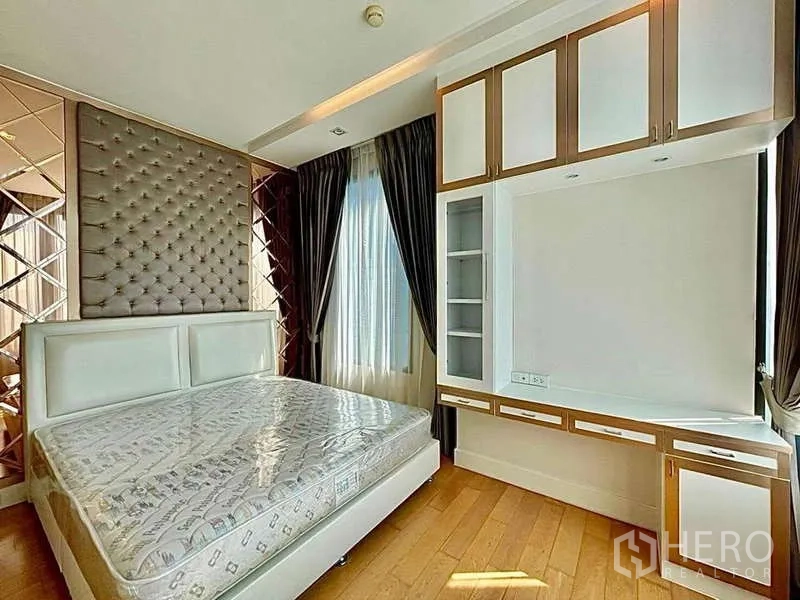 Condominium for rent in Bangkok - Primary bedroom with tufted headboard, built-in shelving and large window.