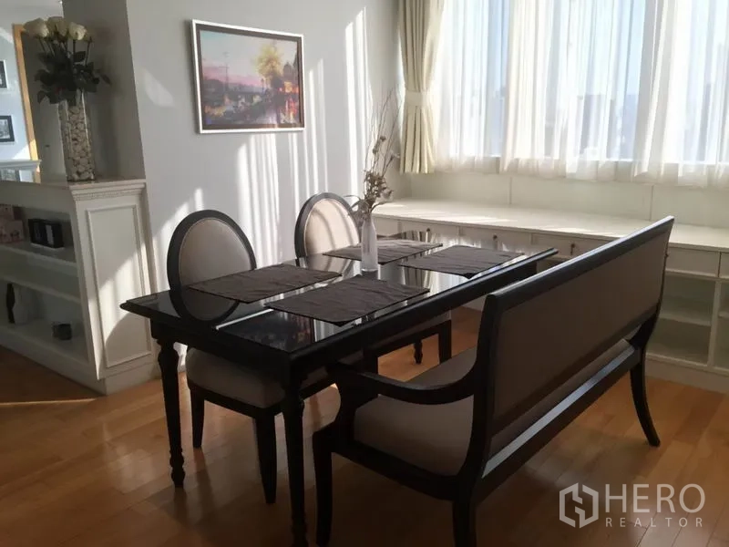 Condominium for rent in Khlong Toei, Bangkok - Dining corner with black glass table, bench seating and wraparound windows with built‑ins.