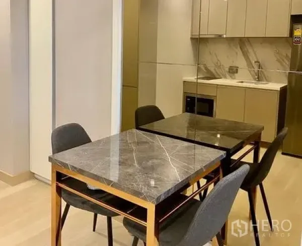 Condominium for rent in Khlong Toei, Bangkok - Dining corner with marble-top table and four dark chairs beside built-in cabinetry.