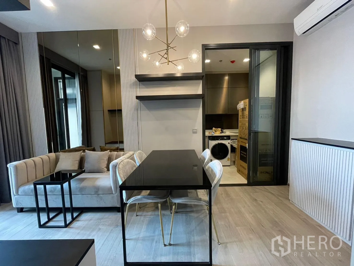 คอนโด for rent in Ratchathewi, Bangkok - ห้องนั่งเล่นและรับประทานอาหารสไตล์โมเดิร์น มีโซฟา โต๊ะอาหารสีดำ โคมไฟทรงกลม และประตูกระจกบานเลื่อนไปยังครัวที่มีเครื่องซักผ้า