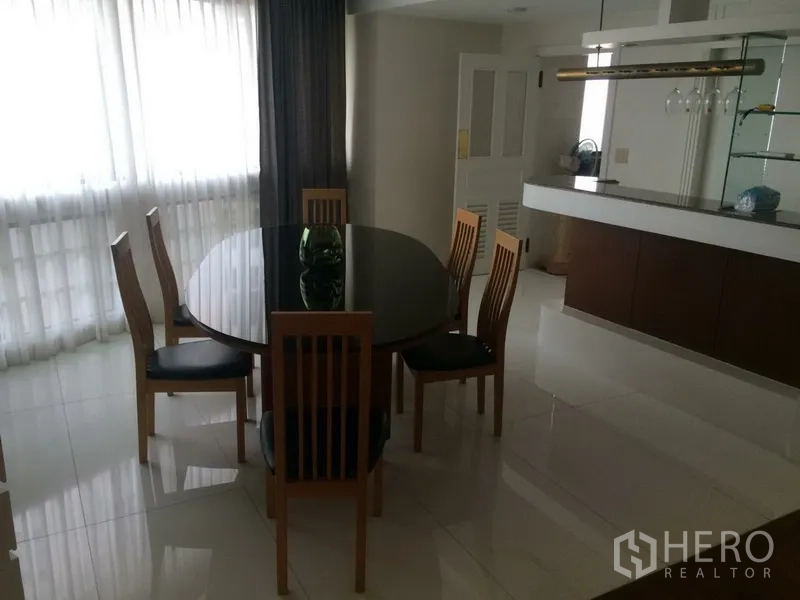 Condominium for rent in Khlong Toei, Bangkok - Bright dining area with a round table for six beside a bar counter and full-height curtains.