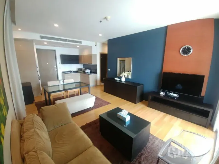 Condominium for rent or sale in Watthana, Bangkok - Open-plan living room with TV feature wall, glass dining table, and warm wood flooring.