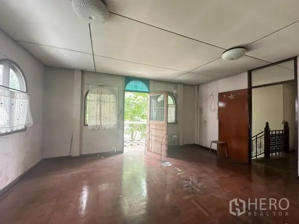 Detached House for sale in Phra Khanong, Bangkok - Spacious empty room with wooden floor, arched windows and a door opening to a small balcony.