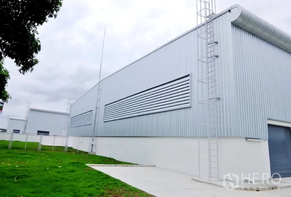 Factory for rent in Bang Sao Thong, Samut Prakan - Modern warehouse façade with ventilation louvers, ladder access and landscaped lawn.