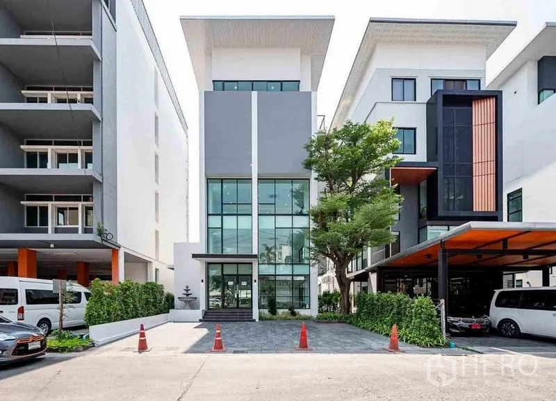 带办公室的家 出租在Suan Luang, Bangkok - 位于曼谷素安隆的现代五层家居办公楼外立面，通高玻璃、车道与绿荫树。