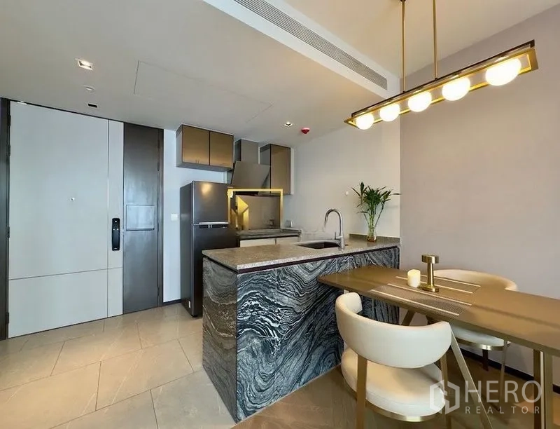 Condominium for rent or sale in Watthana, Bangkok - Contemporary kitchen with patterned stone island, refrigerator, and dining set under pendant light.