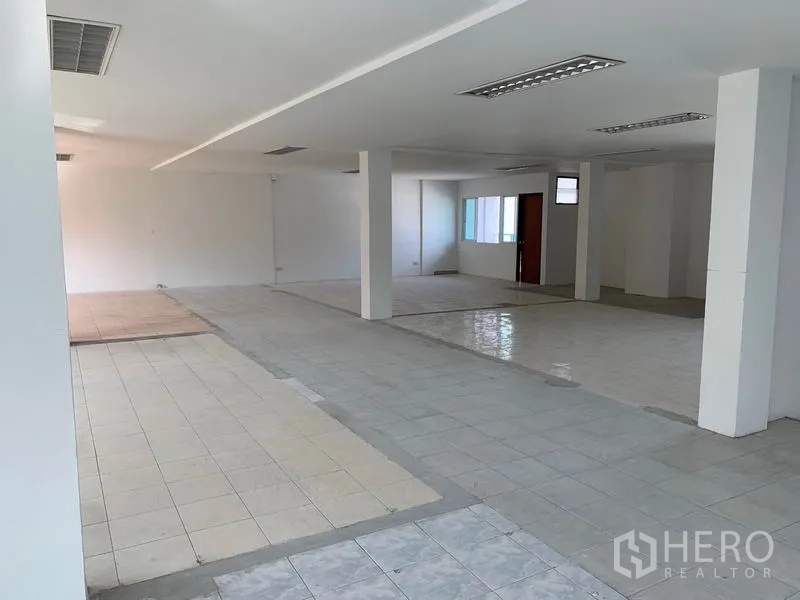 Office Space for rent in Huai Khwang, Bangkok - Wide tiled workspace with fluorescent ceiling lights, windows and an interior doorway.