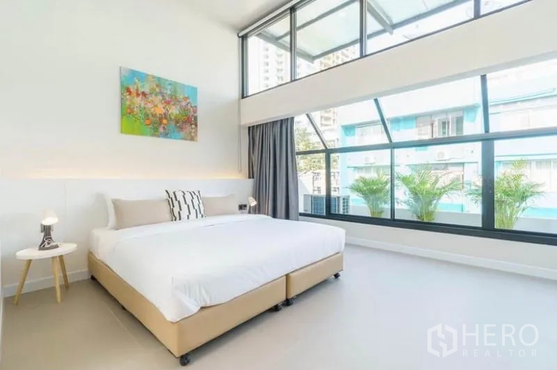 联排别墅 出租在Khlong Toei, Bangkok - 通透明亮的卧室，高挑层高与整面窗墙，阳台绿植
