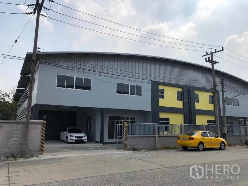 Factory for rent in Lat Lum Kaeo, Pathum Thani - Modern two-storey factory with grey and yellow facade, gated entrance and parking on a wide road in Lat Lum Kaeo, Pathum Thani.