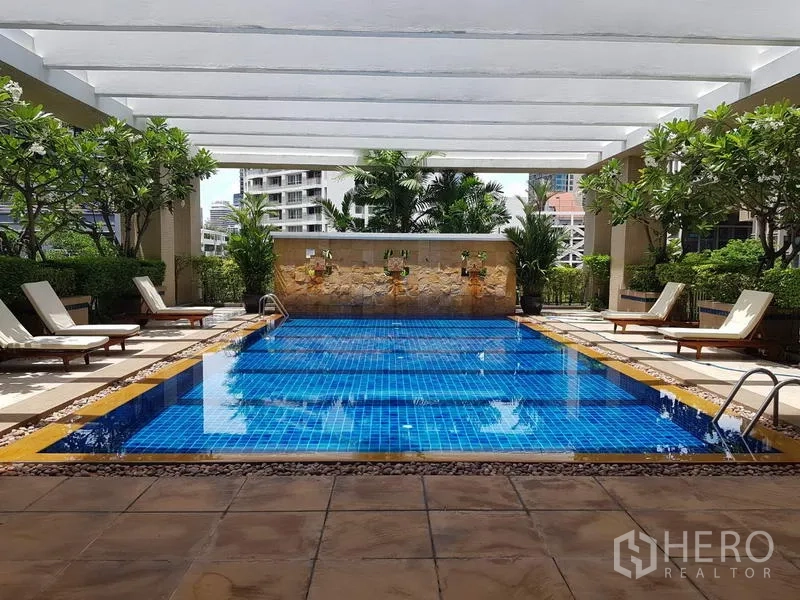 Condominium for rent in Pathum Wan, Bangkok - Condominium swimming pool with blue tiles, sun loungers and landscaped greenery.