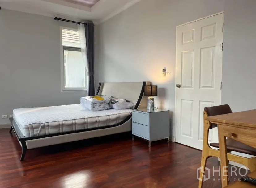 Detached House for rent or sale in Lat Phrao, Bangkok - Spacious master bedroom with bed, bedside lamp and polished wooden flooring.
