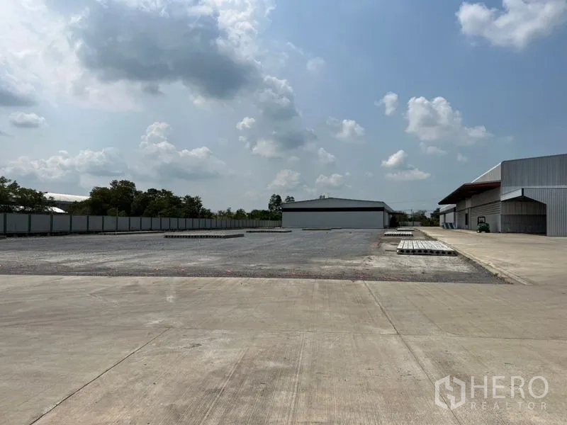 คลังสินค้า ให้เช่าในPathum Thani - ลานคอนกรีตกว้างพร้อมรั้วรอบและอาคารโกดังสมัยใหม่ใต้ท้องฟ้ามีเมฆ