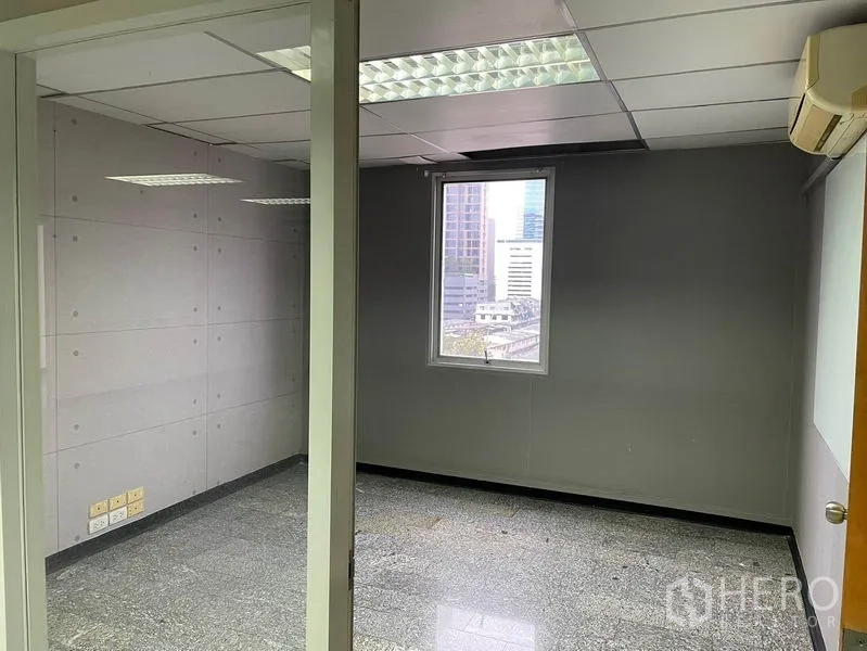 Office Space for rent in Khlong Toei, Bangkok - Glass‑partitioned private office with window views to nearby buildings and ceiling lights.