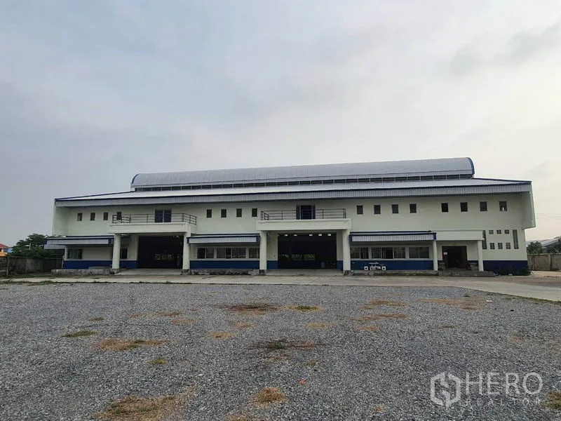 Factory for rent in Bang Bua Thong, Nonthaburi - Symmetrical factory facade with a wide driveway and gravel parking area.