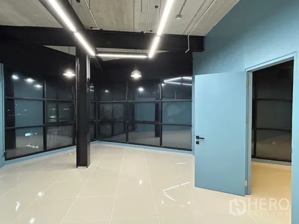 办公空间 出租在Chatuchak, Bangkok - 明亮转角办公室，蓝色门通往相邻房间，环绕式黑框玻璃窗。