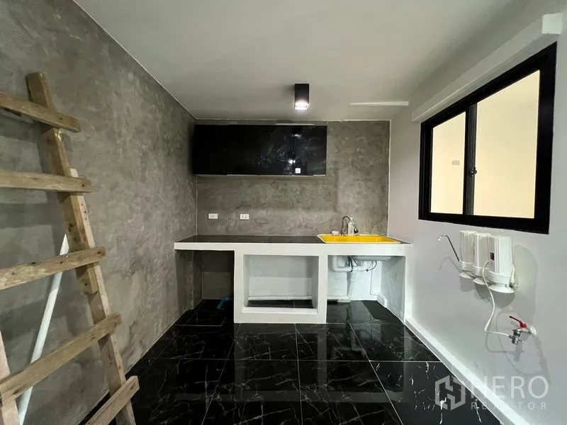 Townhouse for sale in Bang Kapi, Bangkok - Thai-style kitchen with concrete countertop, yellow sink and black marble tiles.