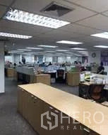 Office Space for rent in Khlong Toei, Bangkok - Open-plan office floor with rows of desks, fluorescent lighting and ceiling air vents with a long storage counter in the foreground.