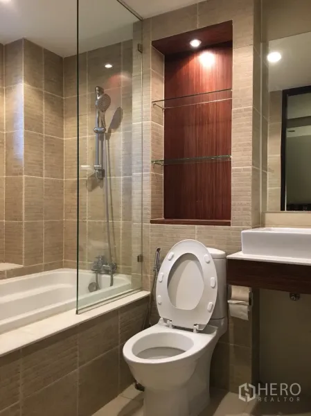 公寓 出租在Watthana, Bangkok - 米色瓷砖卫浴，设浴缸玻璃隔断、手持花洒、坐便和台盆。