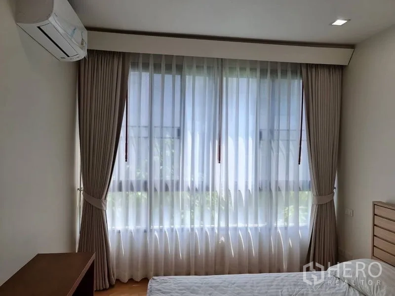 Condominium for sale in Khlong Toei, Bangkok - Bedroom with large curtained window, sheer drapes and air conditioner.