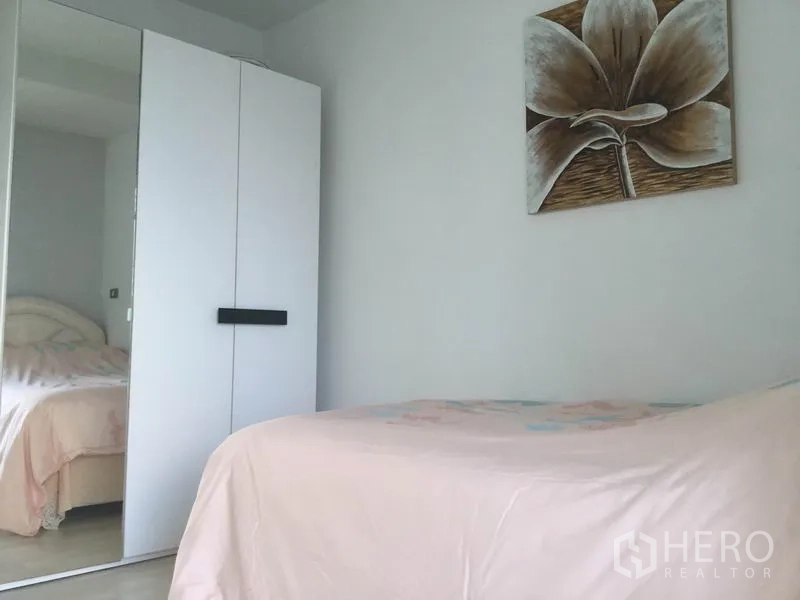 公寓 出租在Watthana, Bangkok - 第二卧室，淡粉色床品，带镜面衣柜，墙上大幅花卉画。