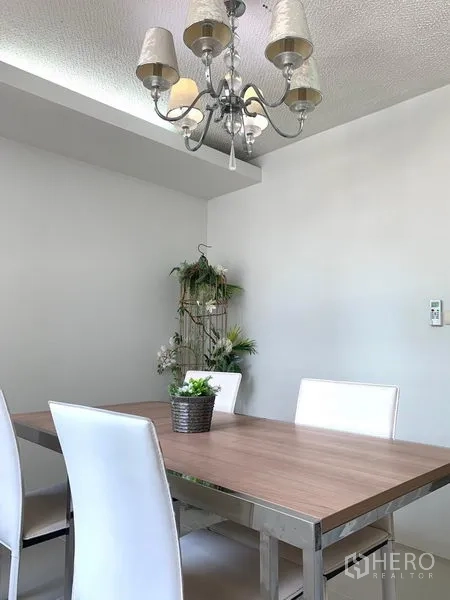 Condominium for rent or sale in Khlong Toei, Bangkok - Dining area with wooden table, white chairs and a chandelier against light gray walls.