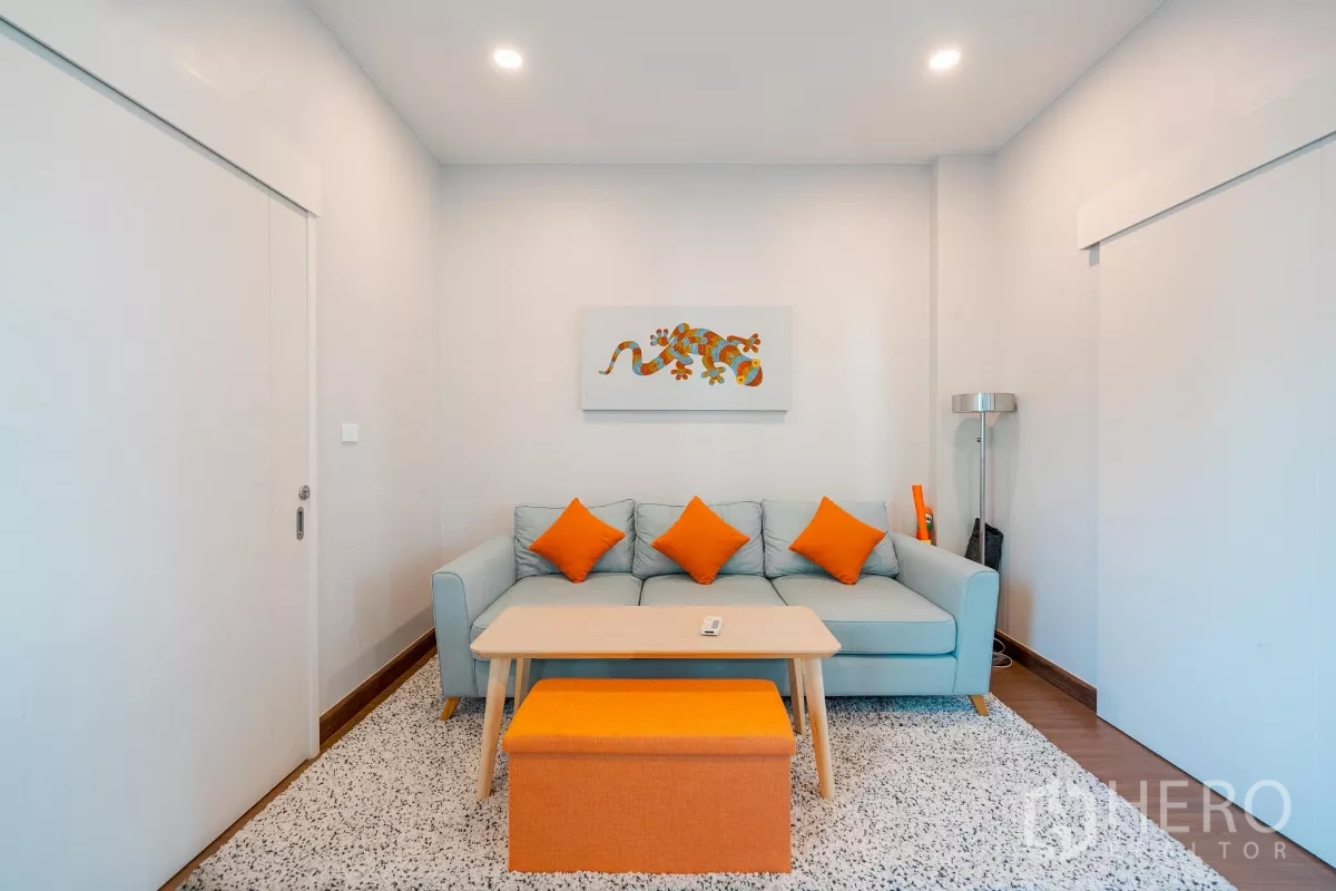 Detached House for sale in Saphan Sung, Bangkok - Cozy multipurpose room with sofa, orange cushions and wall art.